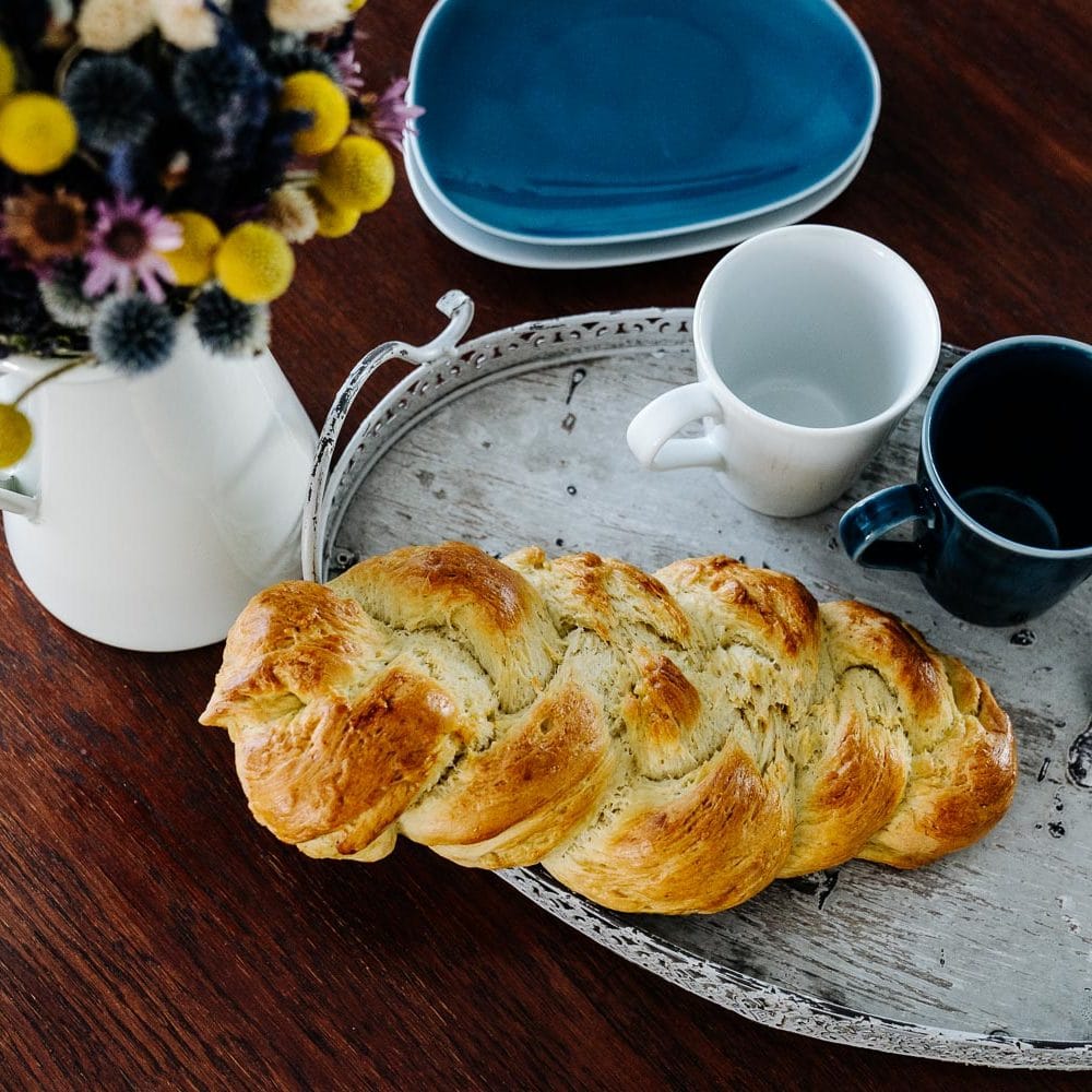 Selbstgemachter Hefezopf auf Tablett mit Teller und Tassen